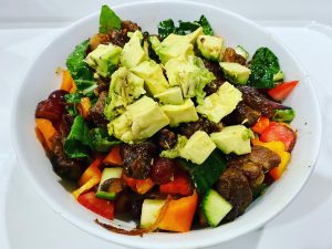 Big bowl of colorful salad topped with meat chunks and avocado cubes